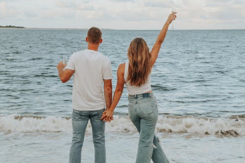 Couple Holding Their Hands and Standing on Seashore Holding a Wine Glass