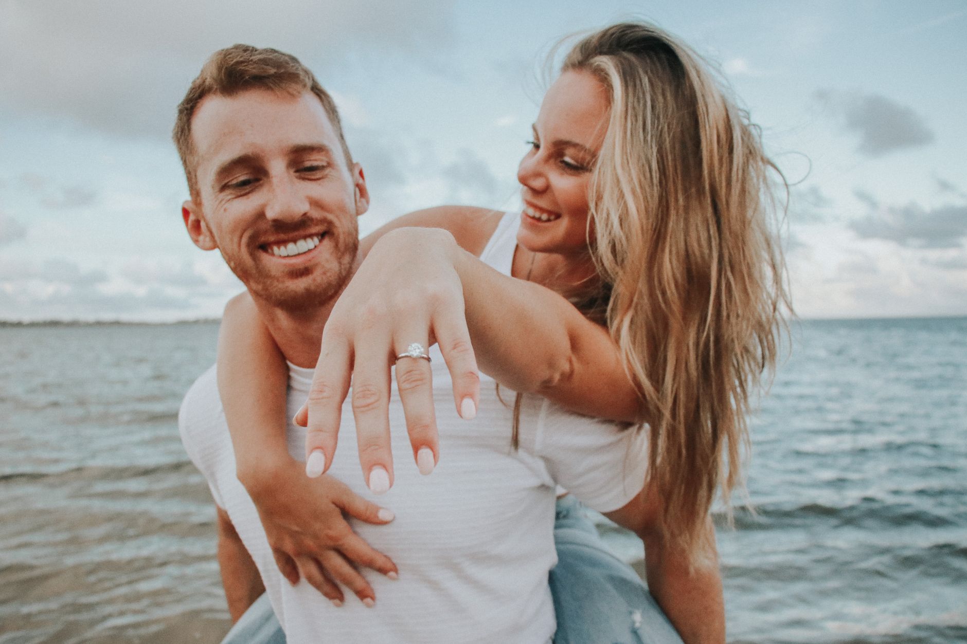 engaged couple celebrating immediately after the proposal - both laughing, champagne visible, ring on her hand, warm outdoor setting