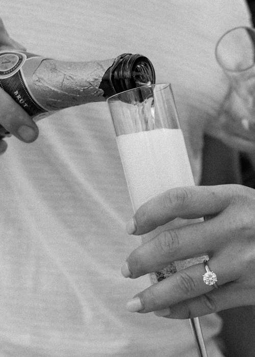 Grayscale Photo of Person Holding Champagne Glass