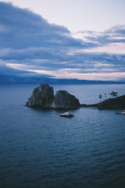 Tranquil view of yacht near rock formations under a dramatic cloudy sky at sea.
