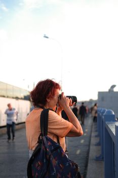 Woman on a bridge with a DSLR camera capturing urban scenery outdoors.