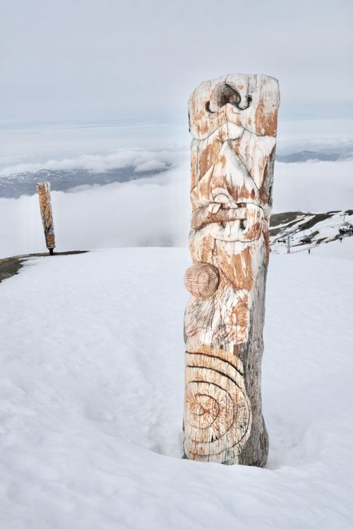 Free A traditional carved wooden sculpture stands amidst a serene snow-covered winter landscape, offering a peaceful view. Stock Photo