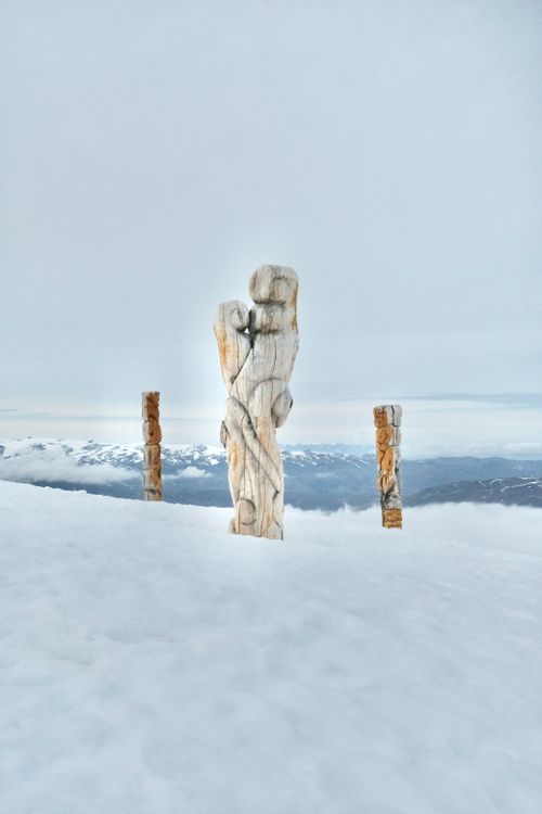 Free Carved wooden statues stand in a serene snow-covered landscape with a winter backdrop. Stock Photo