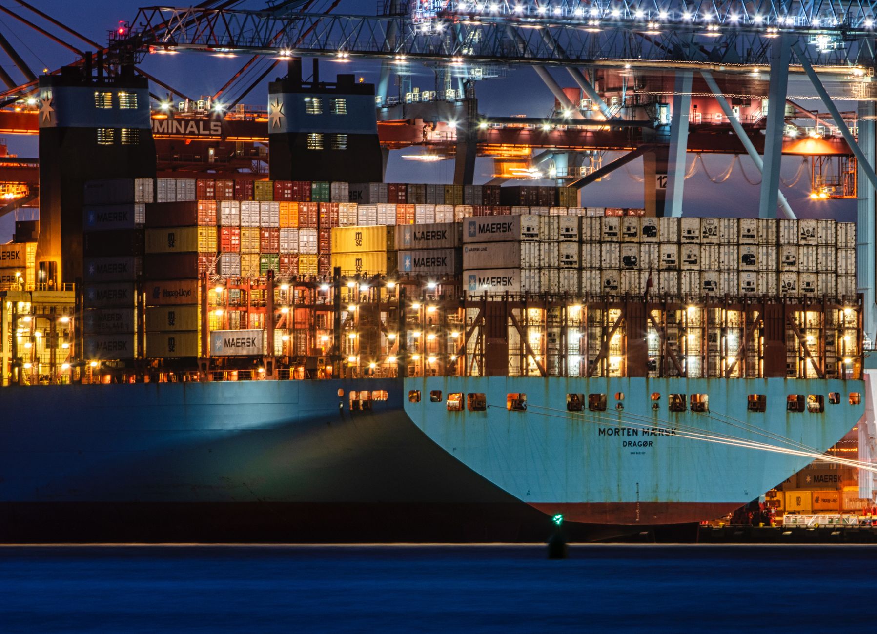 A lit cargo ship loaded with containers docked at Gothenburg harbor, showcasing the bustling night operations.