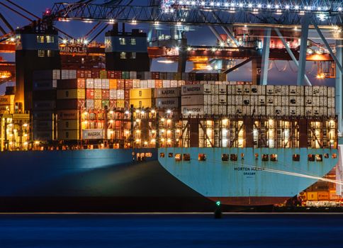 A lit cargo ship loaded with containers docked at Gothenburg harbor, showcasing the bustling night operations.