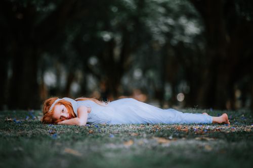 Free A young girl lies on grass in a serene park setting, wearing a white dress, capturing innocence and tranquility. Stock Photo