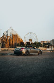 Mercedes Benz sports car parked near a Ferris wheel with a scenic mountain backdrop. Ideal for travel and automotive themes.