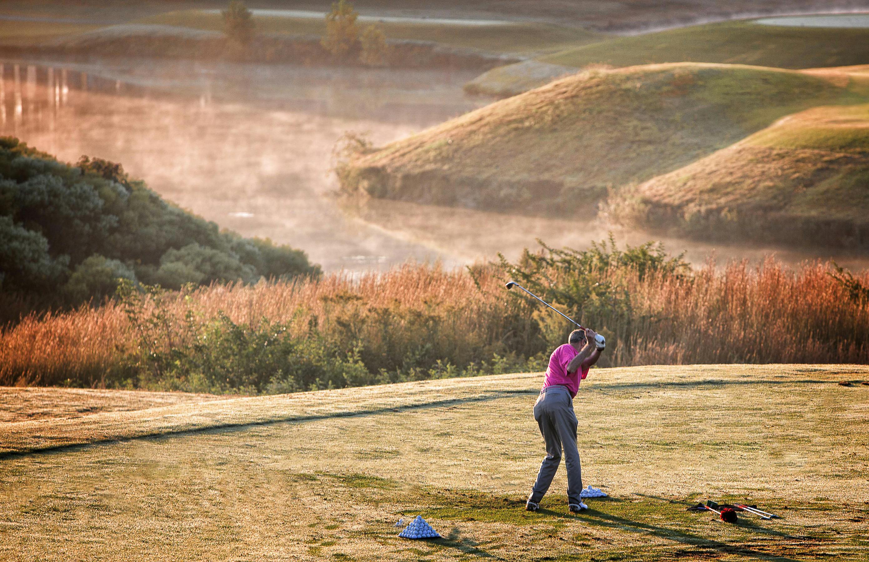Photo of Person Wearing Pink T-shirt and Grey Dress Pants Swinging Golf Club