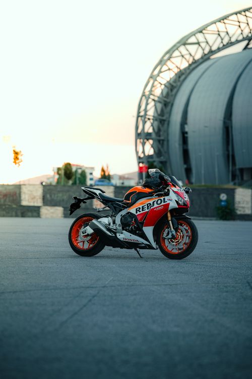 Free A sleek racing motorcycle parked near a futuristic stadium during sunset. Stock Photo