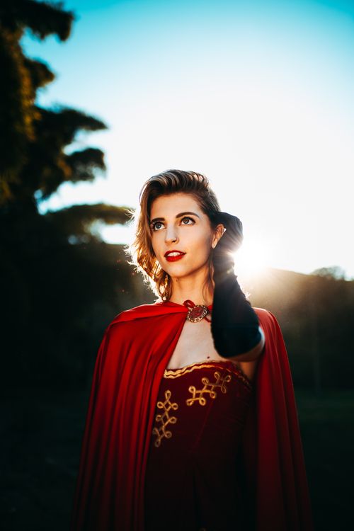 Free Caucasian woman posing in red cloak with long gloves in a vibrant outdoor setting. Stock Photo