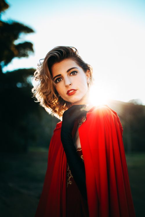 Free Stylish woman in red cape posing with sunlight, outdoors. Fashion portrait capturing elegance and grace. Stock Photo