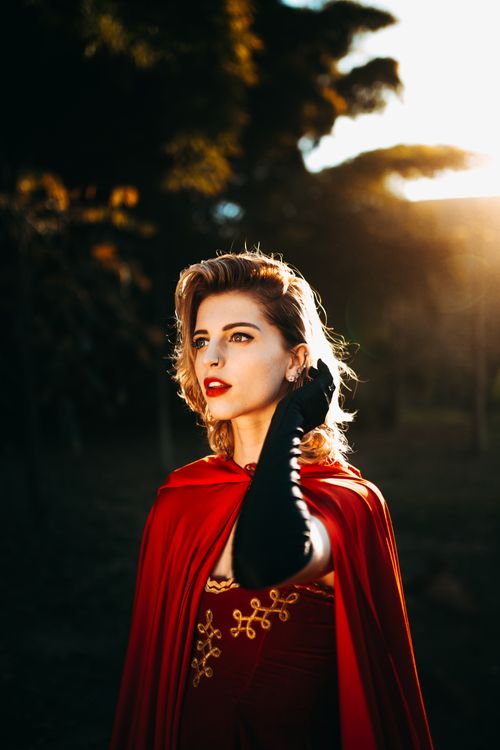 Free Elegant woman in a red cloak posing outdoors during golden hour, exuding vintage glamour. Stock Photo