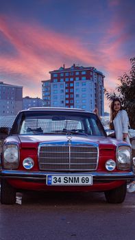 Classic red Mercedes Benz with a woman posing, set against a vibrant twilight urban scene.