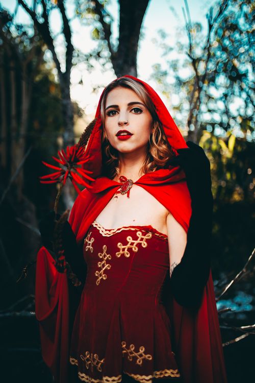 Free Captivating portrait of a woman wearing a vibrant red cape in a forest setting, exuding mystery and allure. Stock Photo
