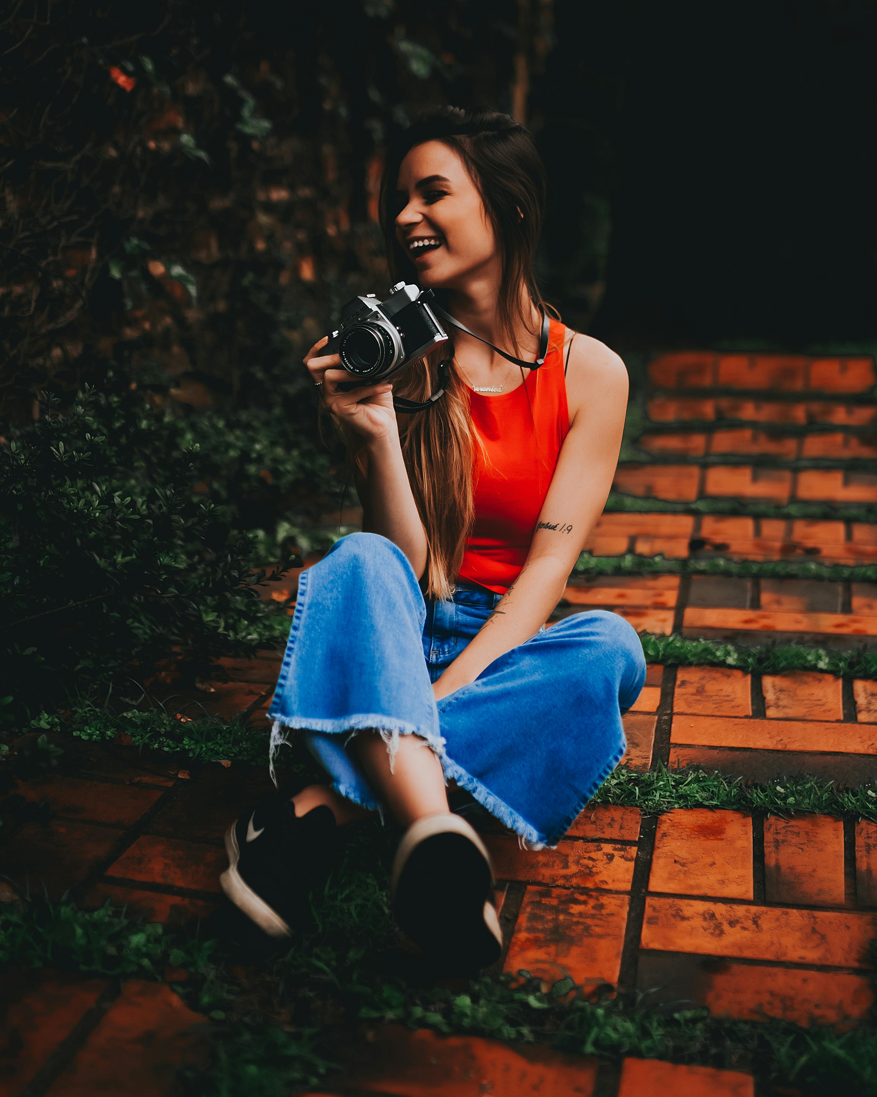 Woman in Red Tank Top and Blue Denim Jeans Sitting on Floor Holding a  Camera · Free Stock Photo