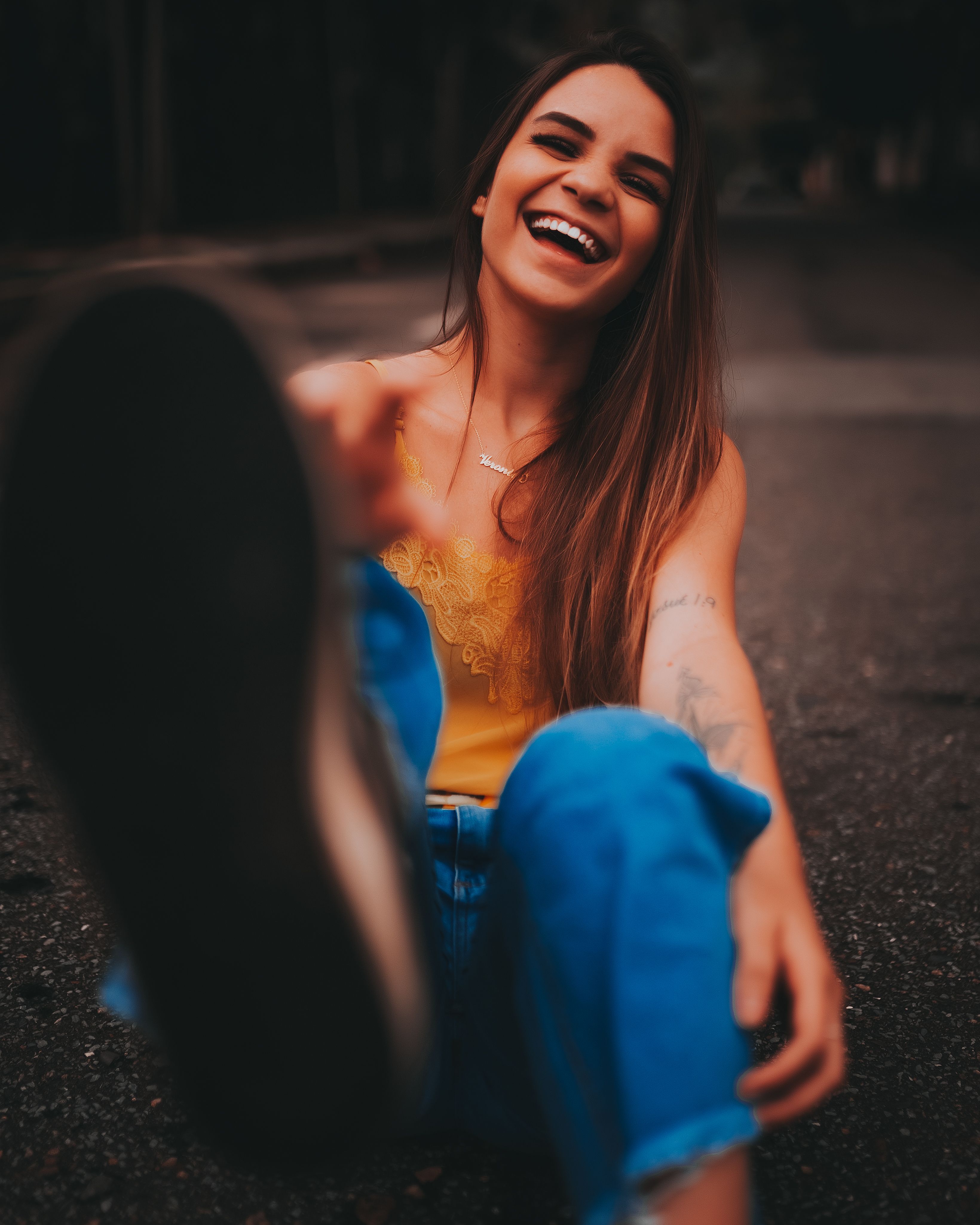 A carefree young woman joyfully laughing while sitting outdoors on a street.