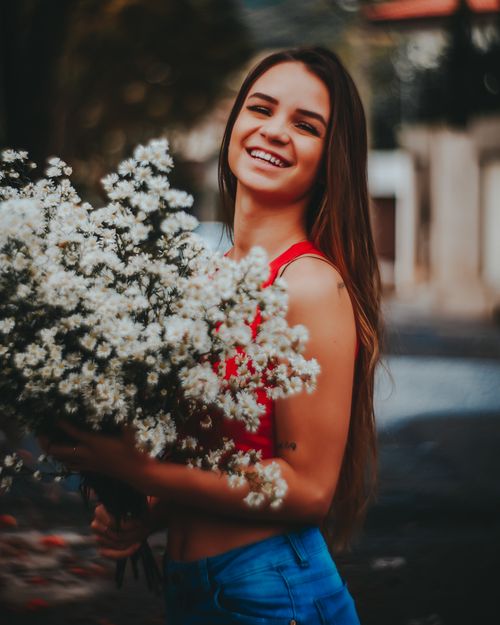 Free Cheerful woman in a red tank top joyfully holding a large bouquet of white flowers outdoors. Stock Photo