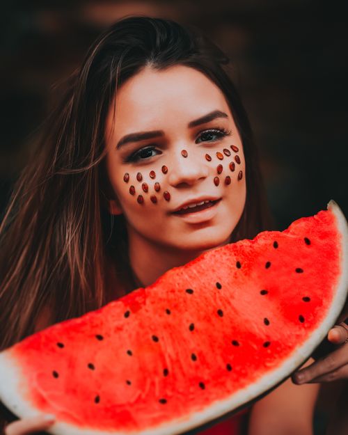 Free Young woman holding watermelon slice with seeds on face, enjoying a fun summer moment. Stock Photo