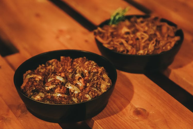 Closeup Of Black Bowls With Meat Dish On A Wooden Table