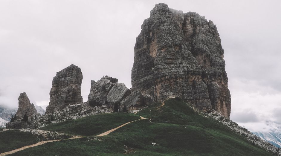 Capture of towering rock formations with a hiking trail in a mountainous landscape under cloudy skies.