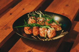 A plate of beautifully presented salmon sushi rolls topped with fresh greens on a wooden table.