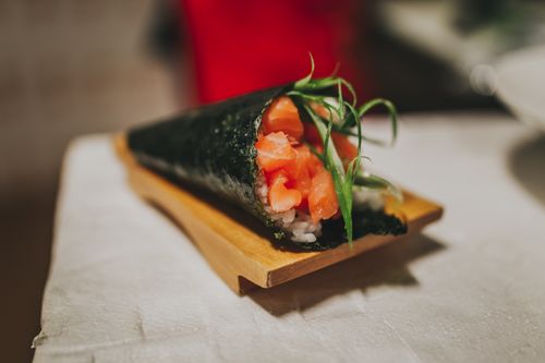 Free Delicious temaki sushi cone with salmon and seaweed on a wooden plate, highlighting Japanese cuisine. Stock Photo