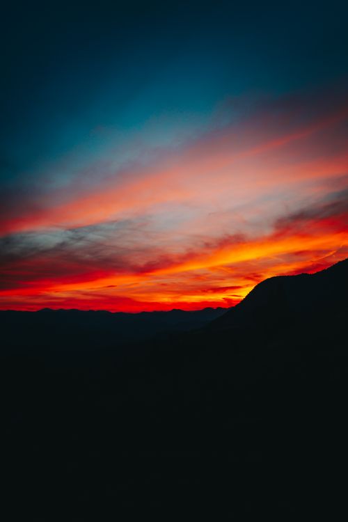 Free Stunning sunset with dramatic clouds over silhouetted mountains, creating a vibrant and colorful sky. Stock Photo