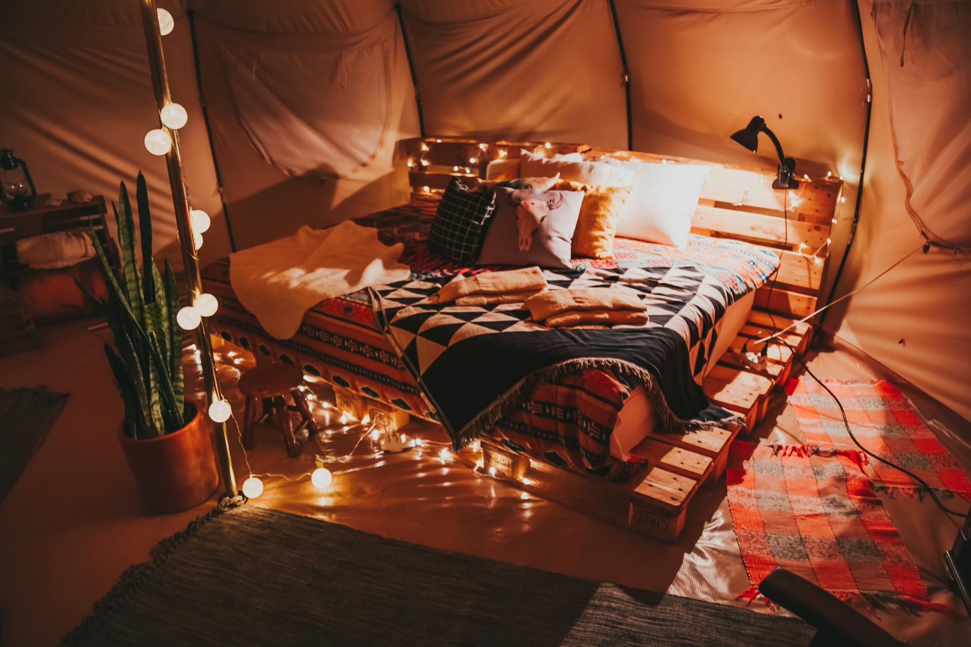 A cozy indoor tent featuring a pallet bed, warm lighting, and decorative pillows for ultimate comfort.