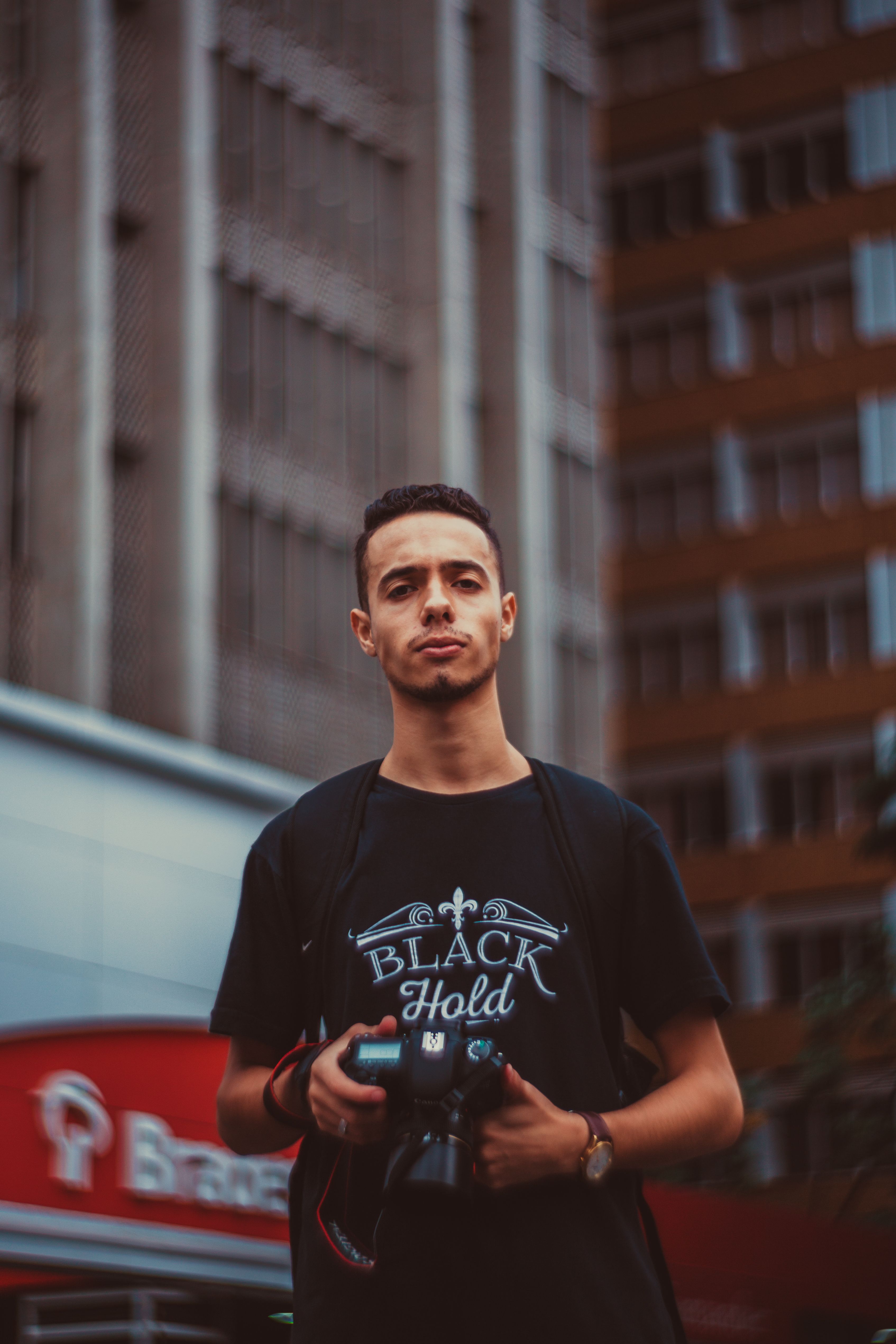 Portrait of a young man holding a camera on a city street.