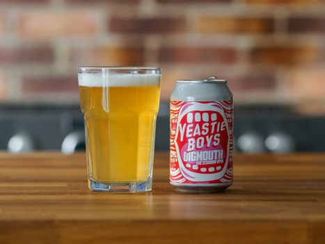 Close-up of Yeastie Boys Bigmouth IPA can with beer glass on wooden table.