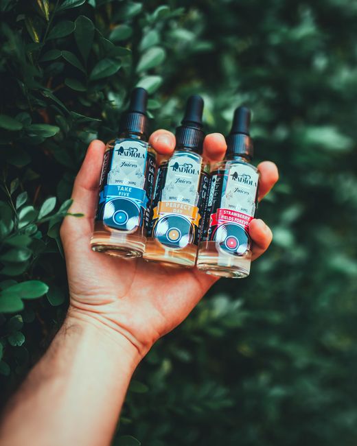 A close-up of a hand holding three Radiola vape juice bottles against a leafy background.