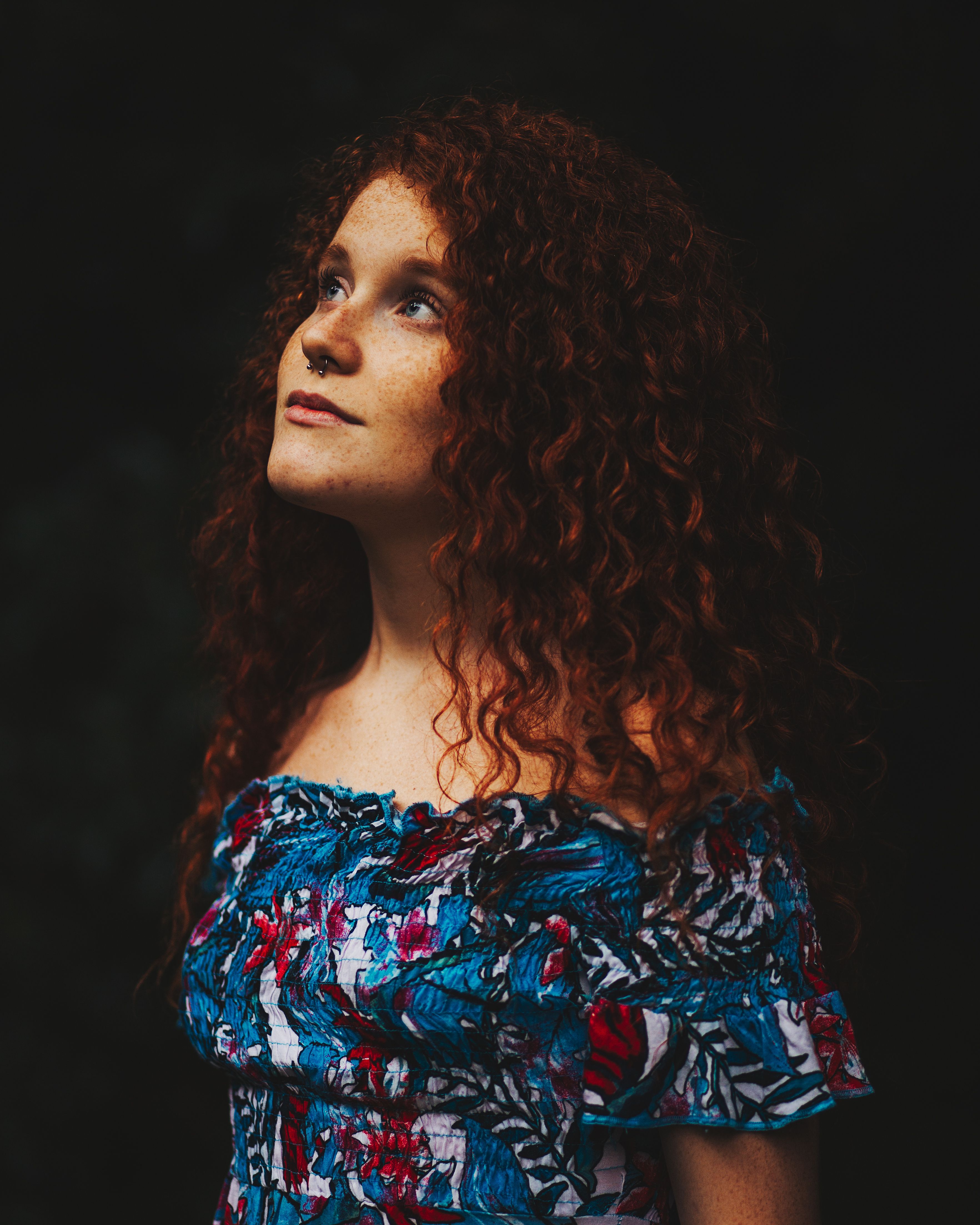 A young woman with curly red hair gazes upward, captured in a moody, artistic portrait.