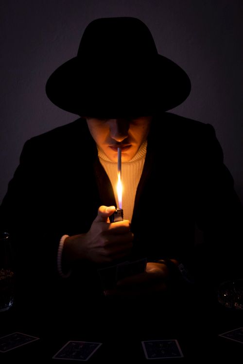 Free A person with a black hat lights a cigarette in a dark, moody setting. Stock Photo