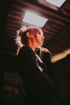 A contemplative woman with hair lit by sunlight stands in a loft-like space.