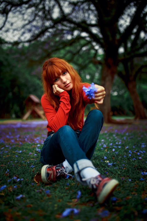 A Young Woman in Red Long Sleeves Holding a Flower while Sitting at a Park