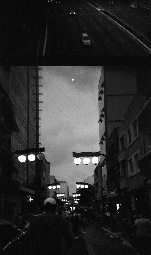 Free A bustling city street at night with pedestrians and streetlights in black and white. Stock Photo