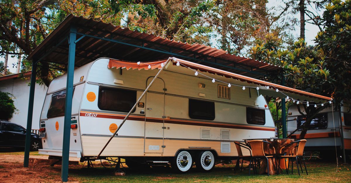 Relaxing motorhome camping setup with chairs and table in a scenic summer forest setting.