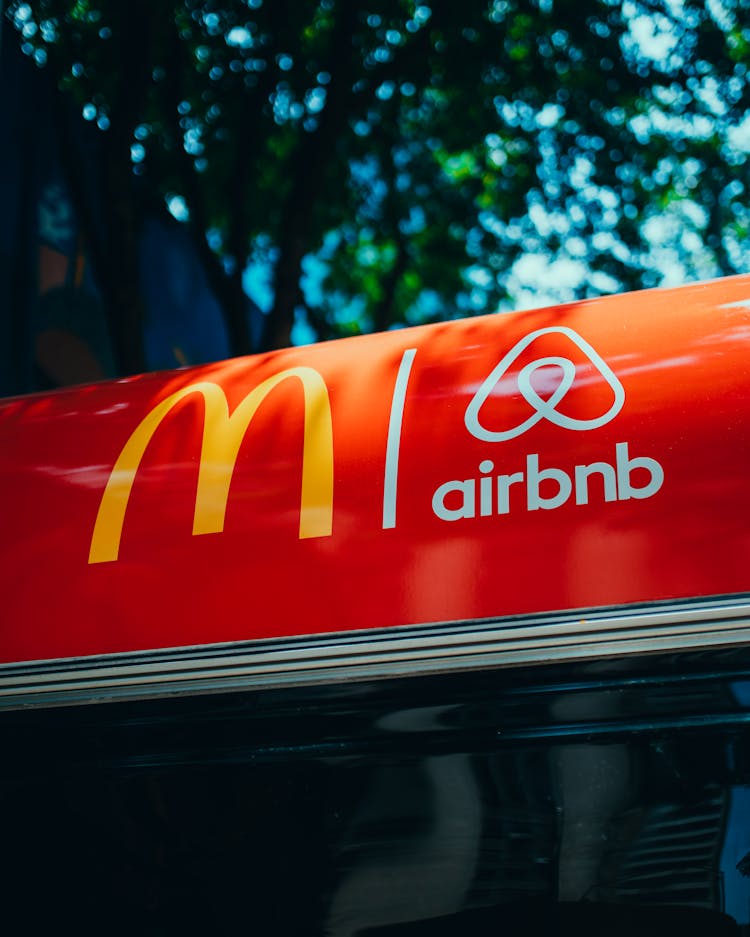 Two Logos On A Red Surface, And Tree In Background