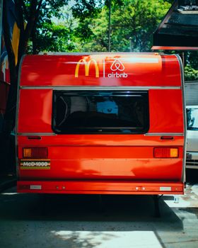 Vibrant red camper van in a city location featuring McDonald's and Airbnb logos. 13870637