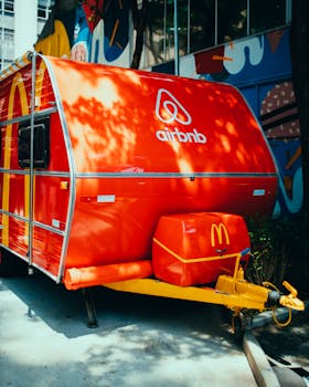 Brightly painted Airbnb branded food truck parked in a vibrant urban area with street art backdrop.