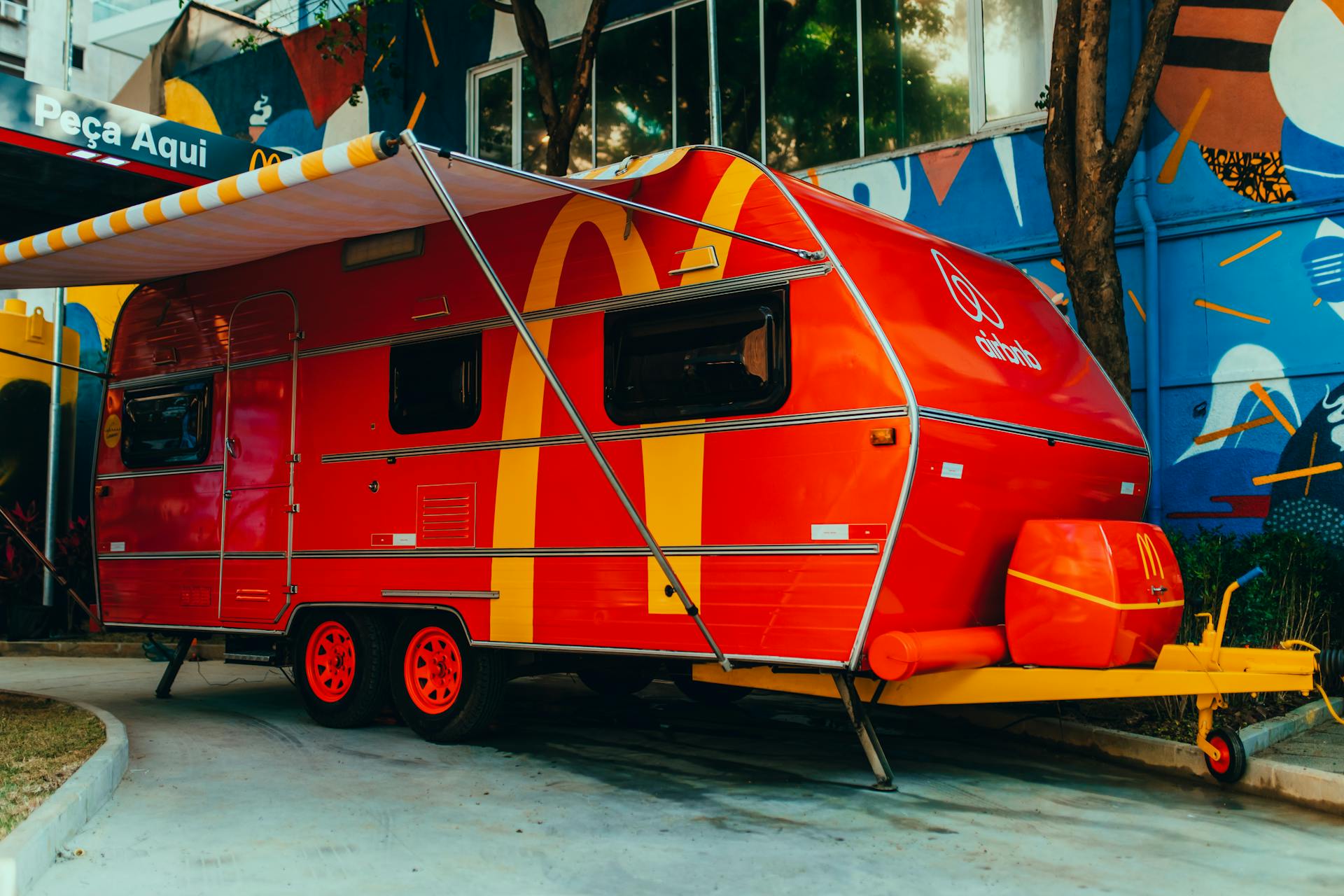Bright red camper trailer with yellow designs parked on a colorful street. Ideal for travel themes.