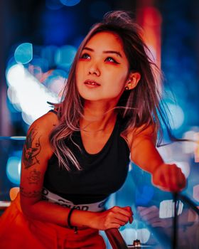 Striking young woman poses under vivid city lights at night, exuding modern elegance.