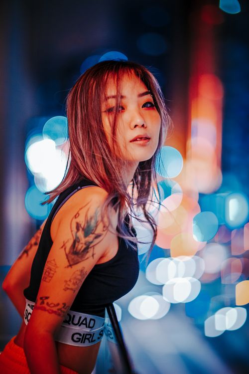 Free A trendy woman with tattoos posing against a colorful city night backdrop, exuding urban style. Stock Photo