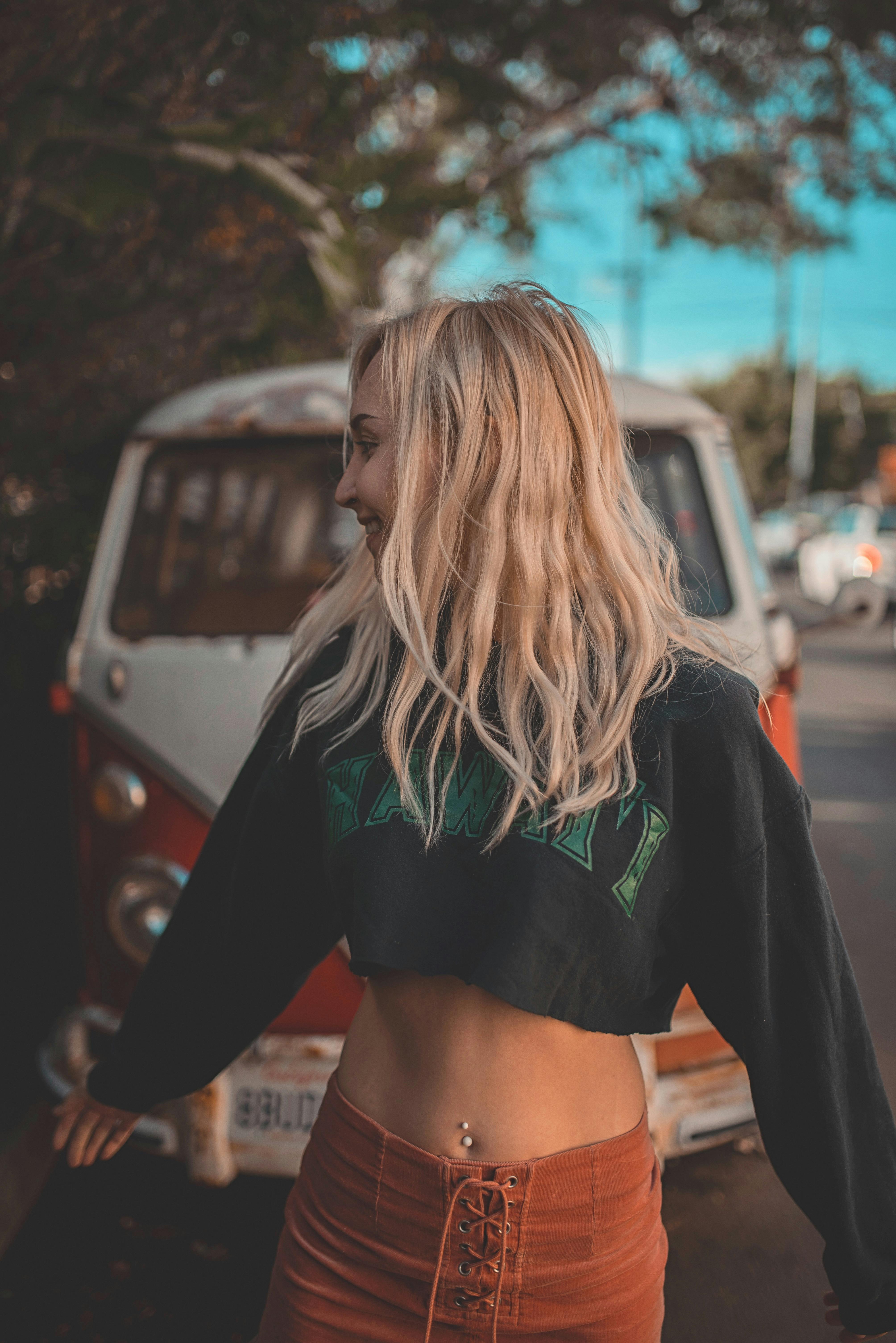 Blonde woman posing stylishly with a vintage van outside on a sunny day.