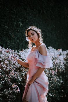 Elegant woman posing in pink dress surrounded by flowers, showcasing fashion and nature.