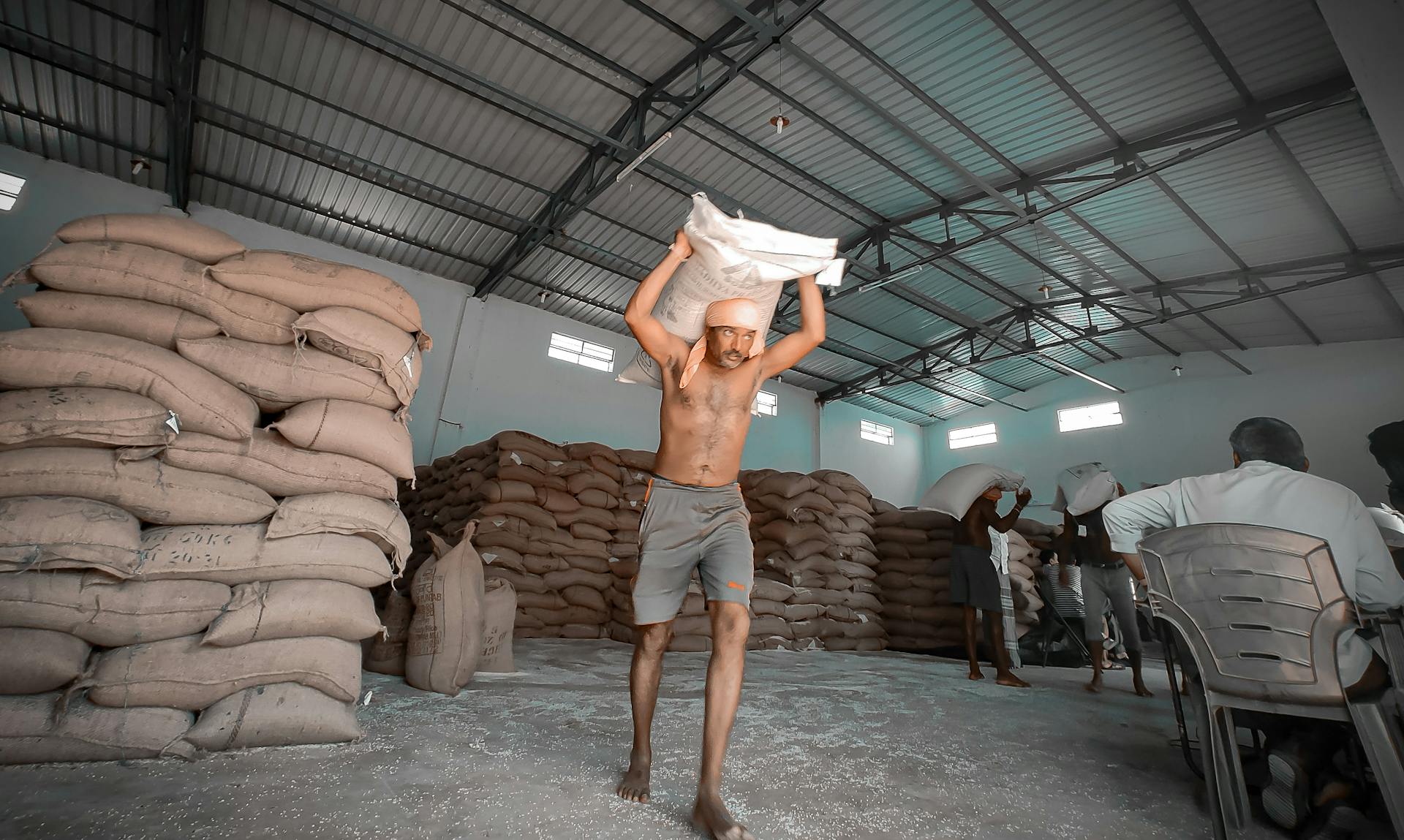Men working shirtless in a warehouse, carrying sacks of flour for packaging.