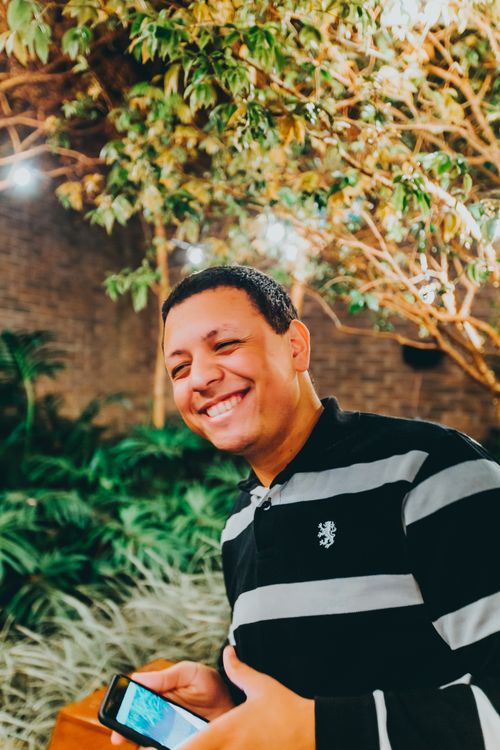 Free Cheerful man with smartphone smiles in lush, well-lit indoor garden. Stock Photo