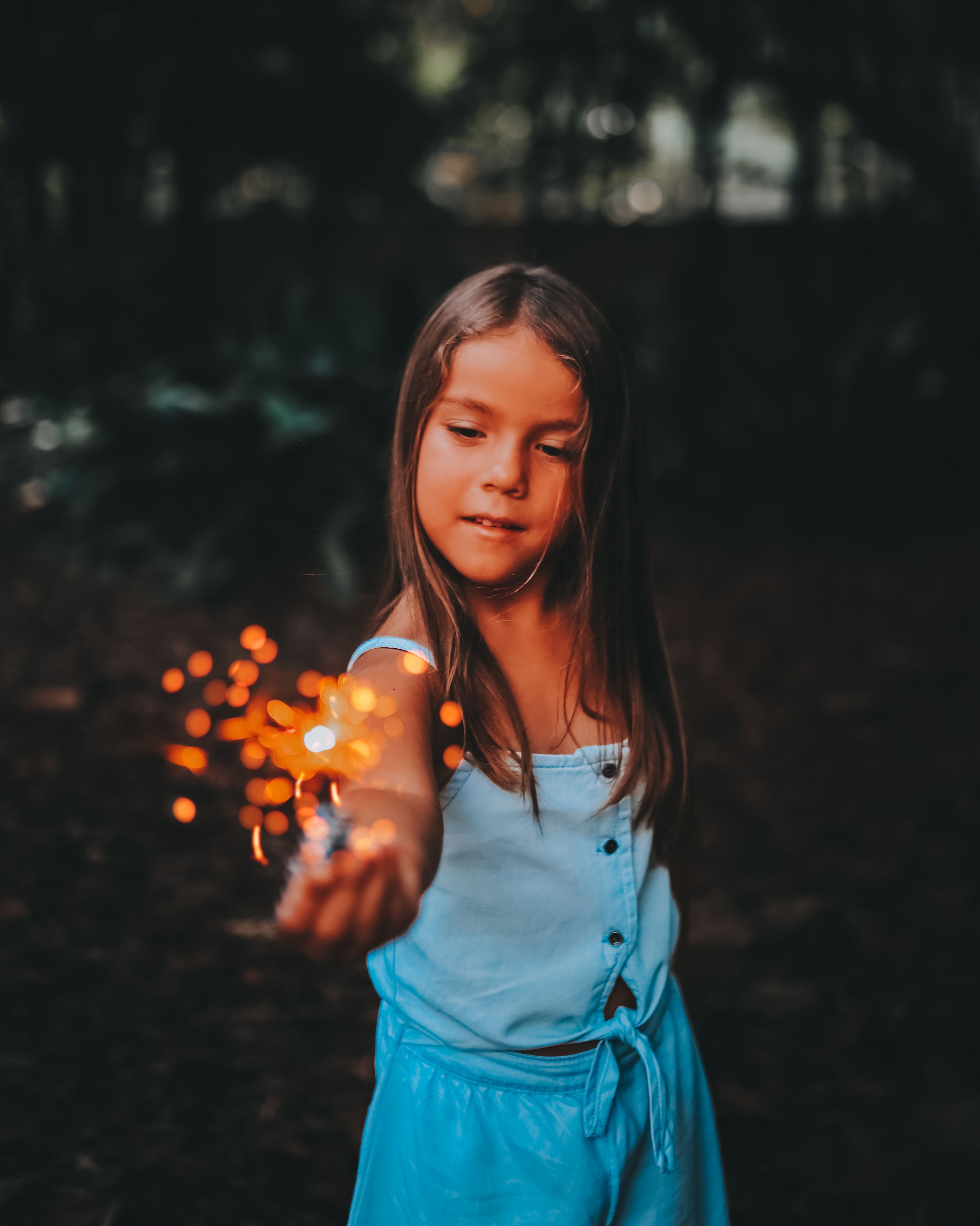 A young girl holding a sparkler, creating a magical atmosphere in the night outdoors.