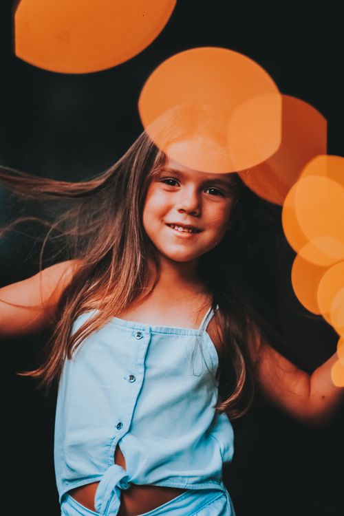 Free Cheerful girl smiling with playful orange light bokeh effects in a stylish portrait. Stock Photo