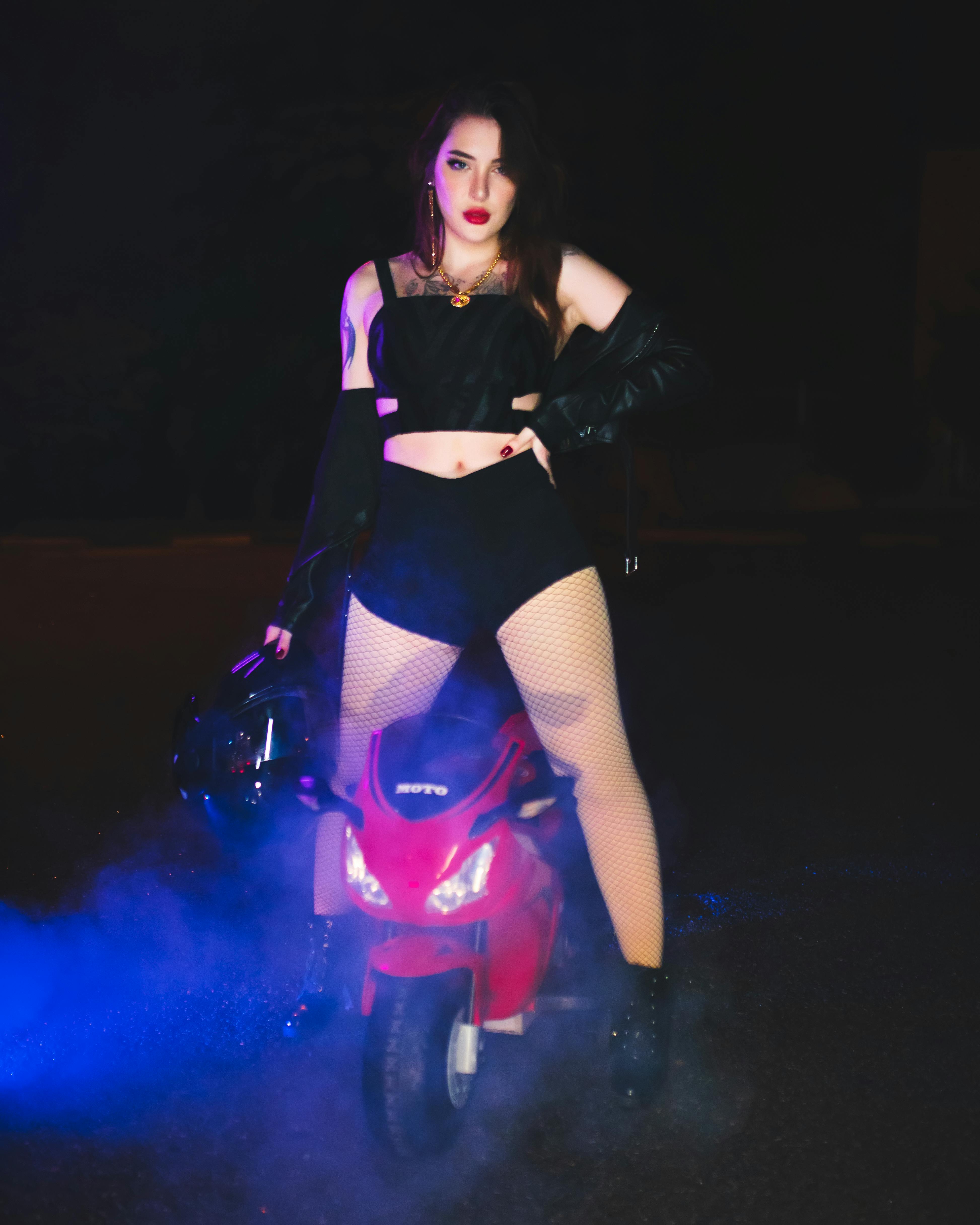 Portrait of fashionably dressed woman posing with a motorcycle at night.